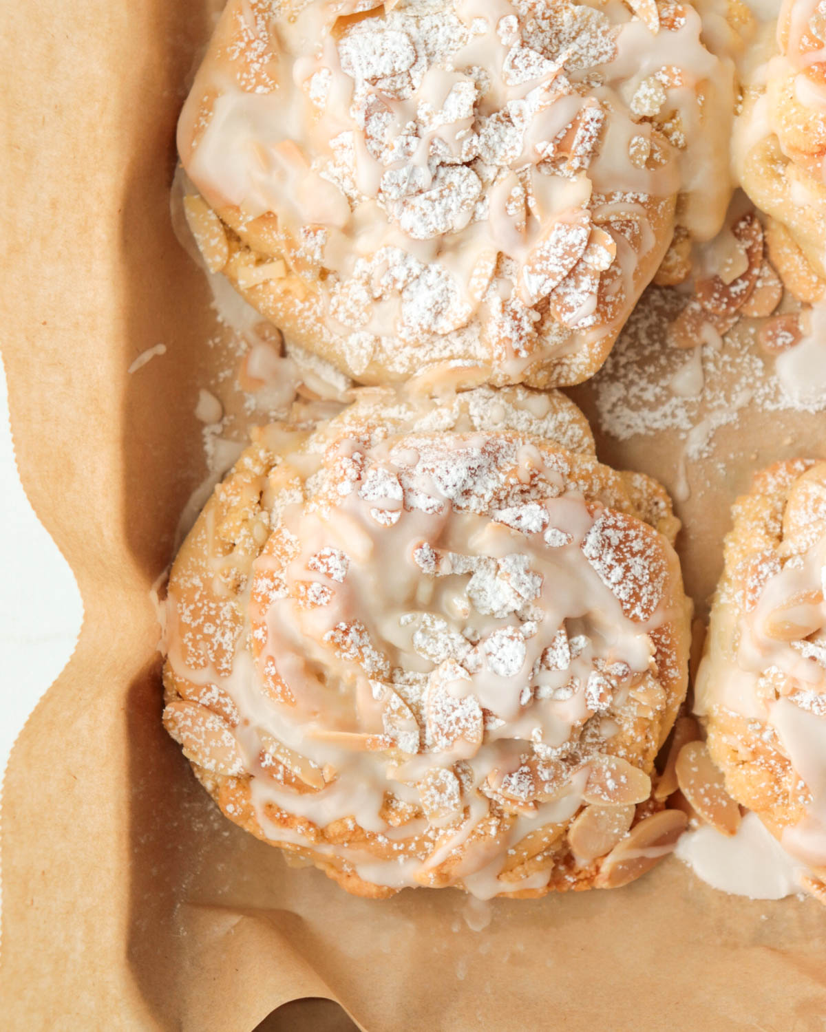 Almond buns on a baking pan topped with powdered sugar and icing.
