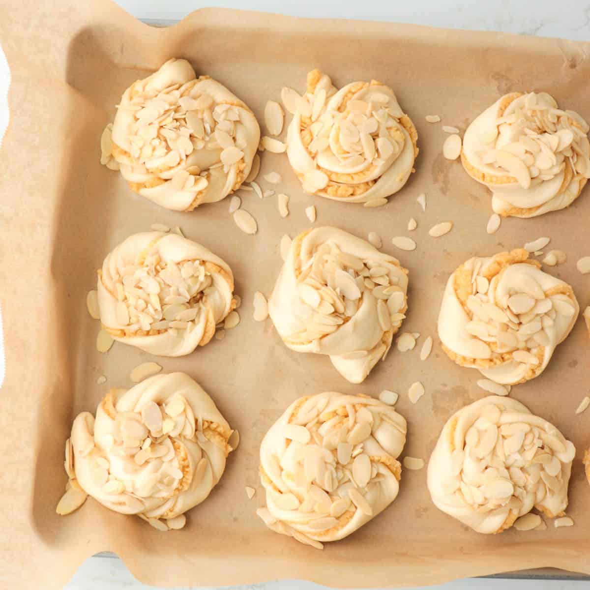 Risen buns with sliced almonds on top before baking.