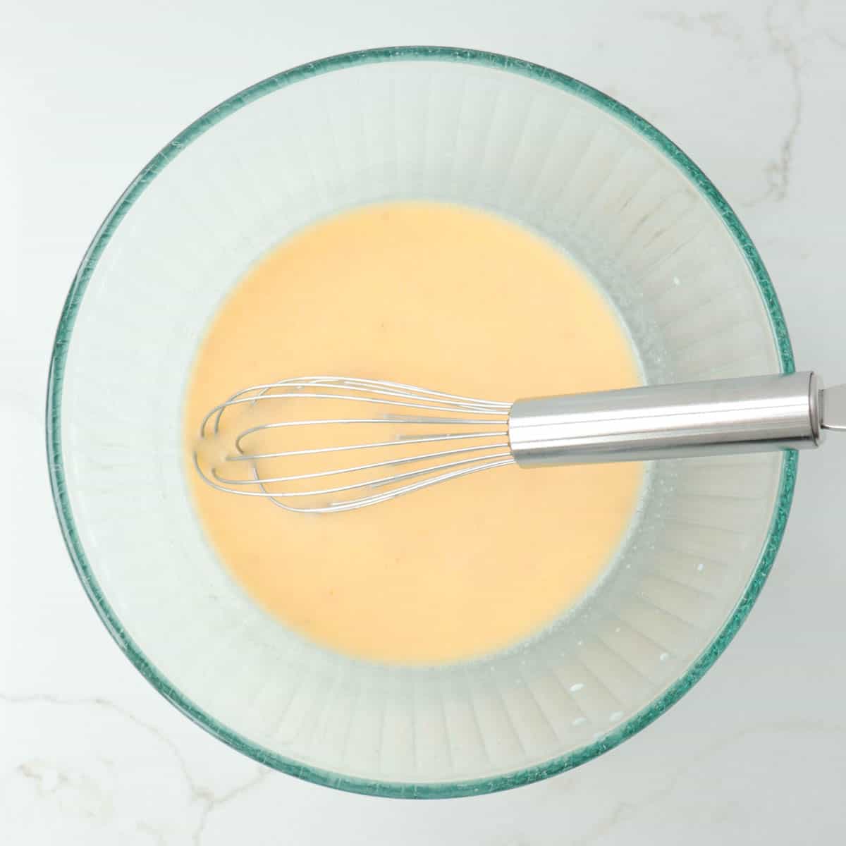 Wet ingredients for dough mixed with yeast in glass mixing bowl.